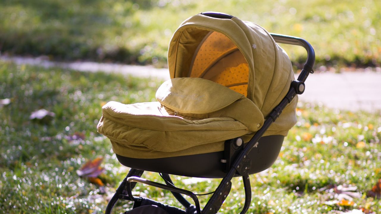 A yellow baby stroller standing on a lawn covered in autumn leaves