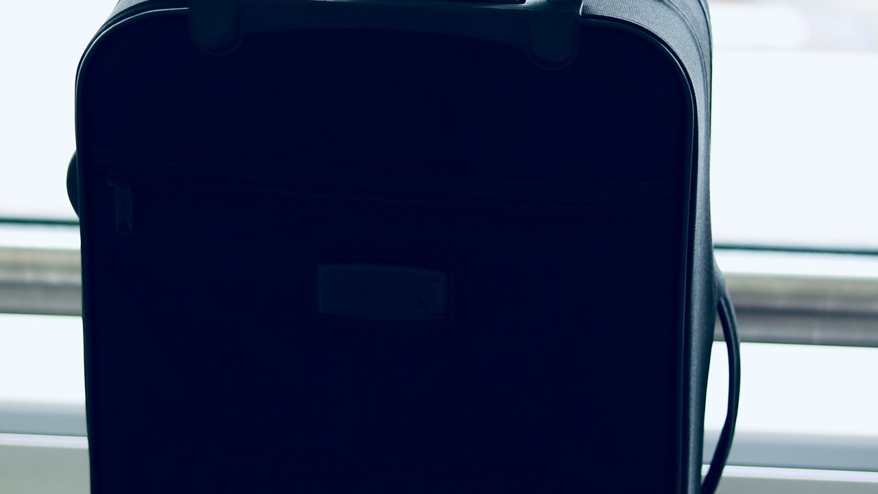 A black suitcase with a luggage tag standing in a bright airport window